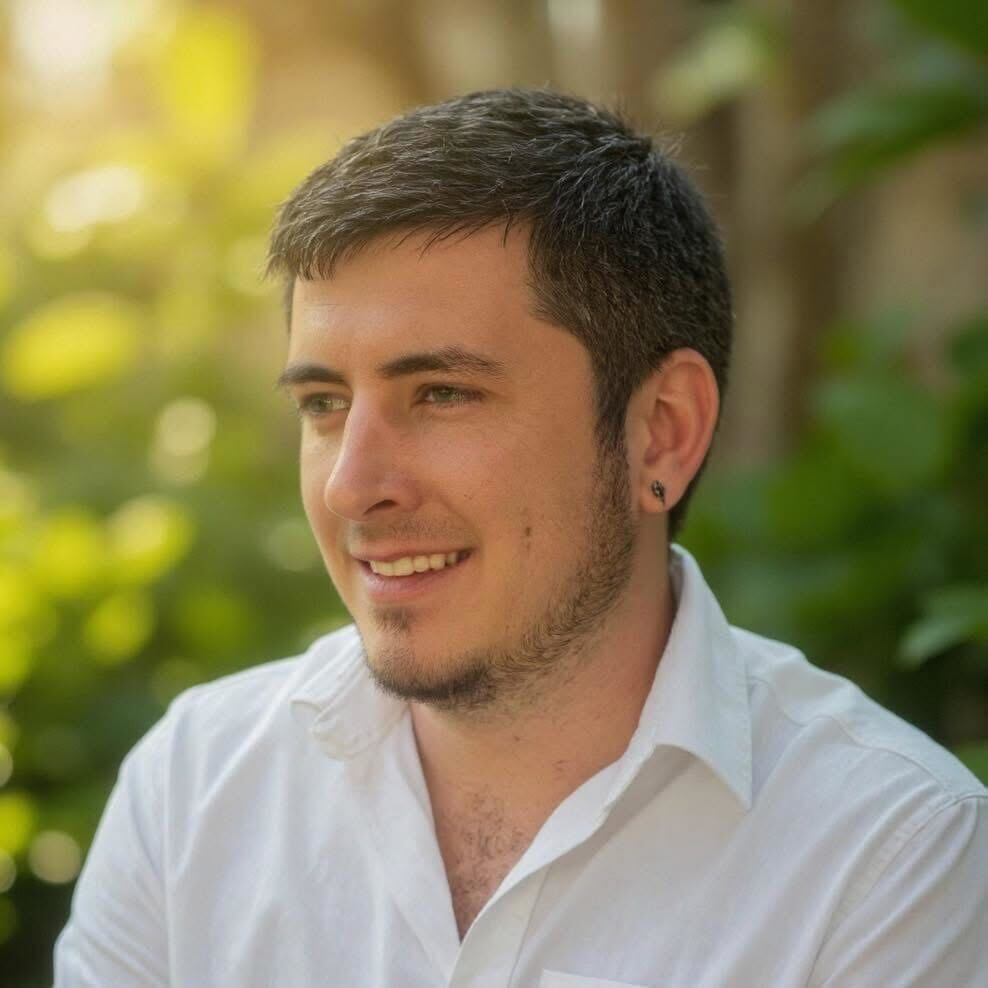Garrett Shingler smiling in a white shirt, sunlit greenery behind him